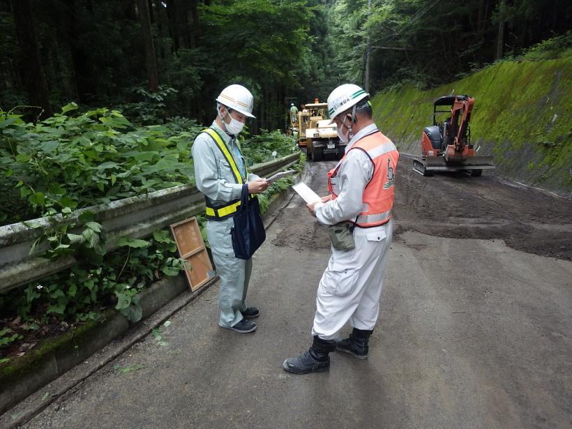 道路工事の現場で状況の確認をしている渡邉技師と作業員の写真